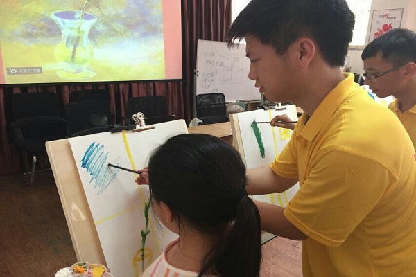 20160717131922703827.jpg 志愿队员在帮助孩子画油彩画.jpg